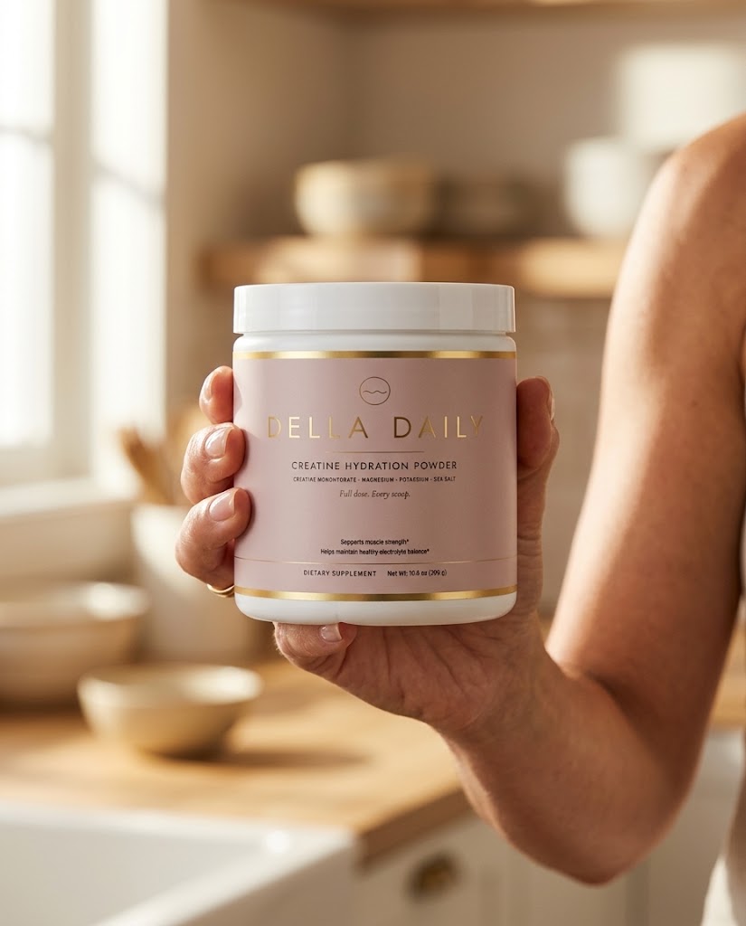 Hand holding a 30-serving tub of Della Daily creatine hydration powder